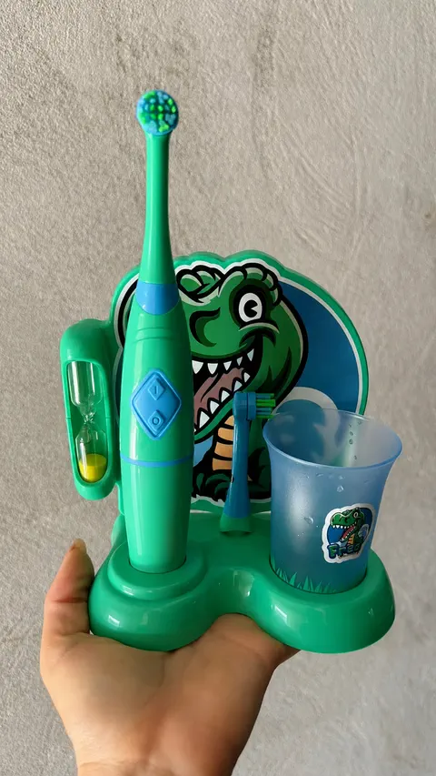 Kit verde segurado na mão, mostrando a ampulheta de areia, a escova, a cabeça de reposição e o copo